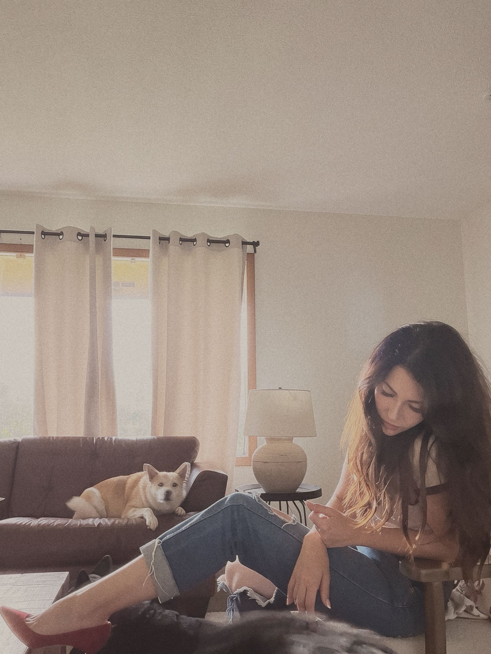 Sandra sitting in her living room looking down at her hands, her dog lying on the brown couch behind her.