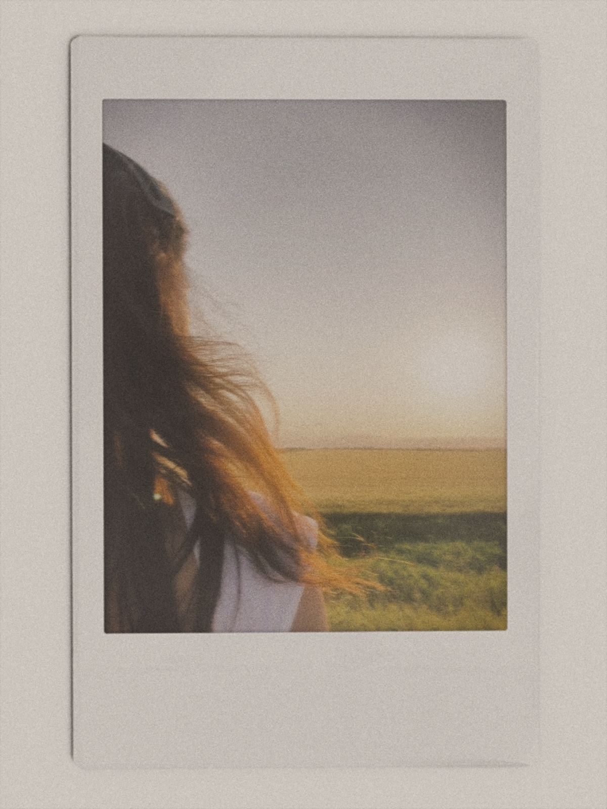 An instant-film photograph of a woman looking out over a field at sunset.