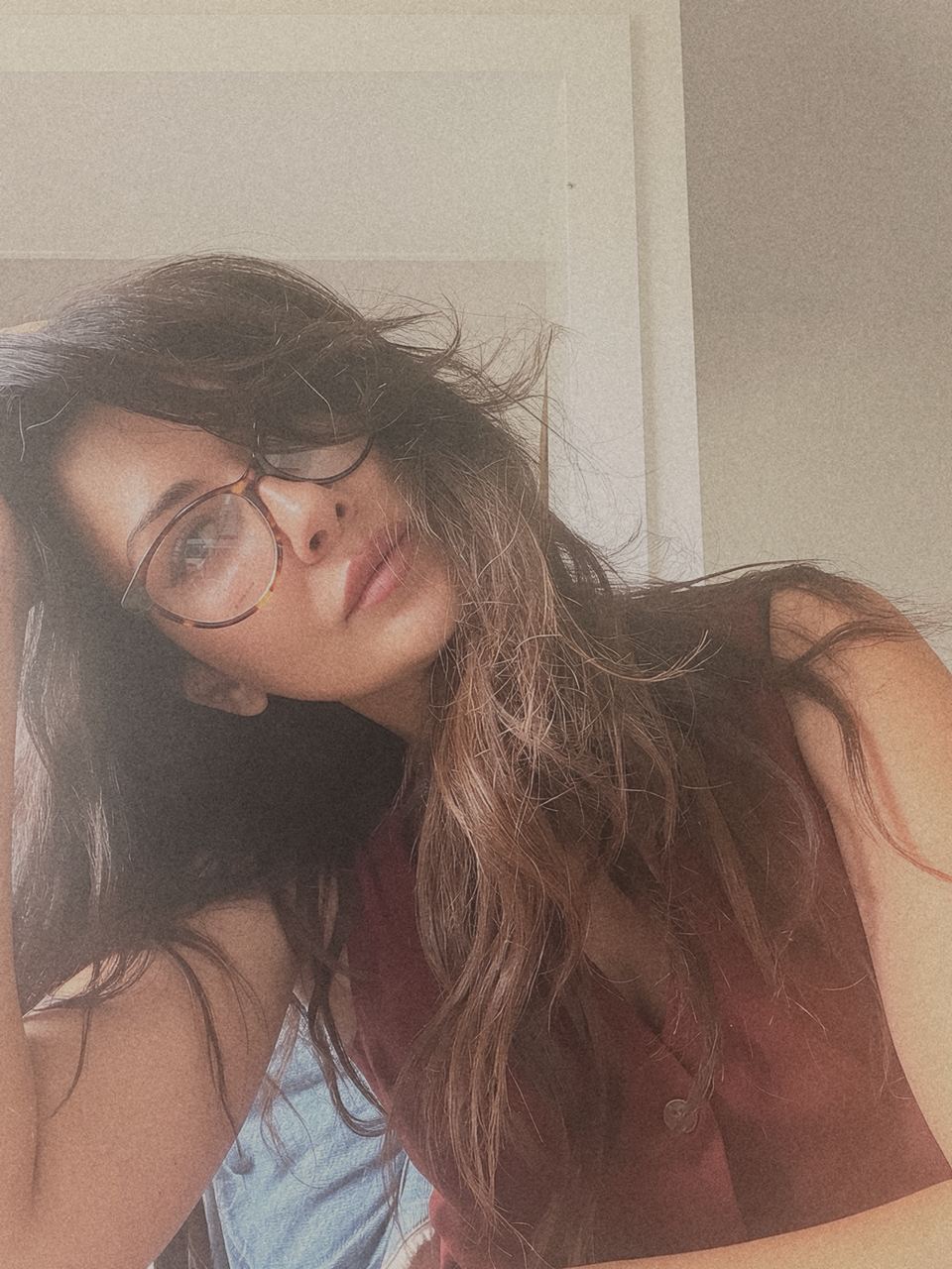 Sandra in round tortoiseshell glasses, her head tilted and resting on her hand, looking at the camera.